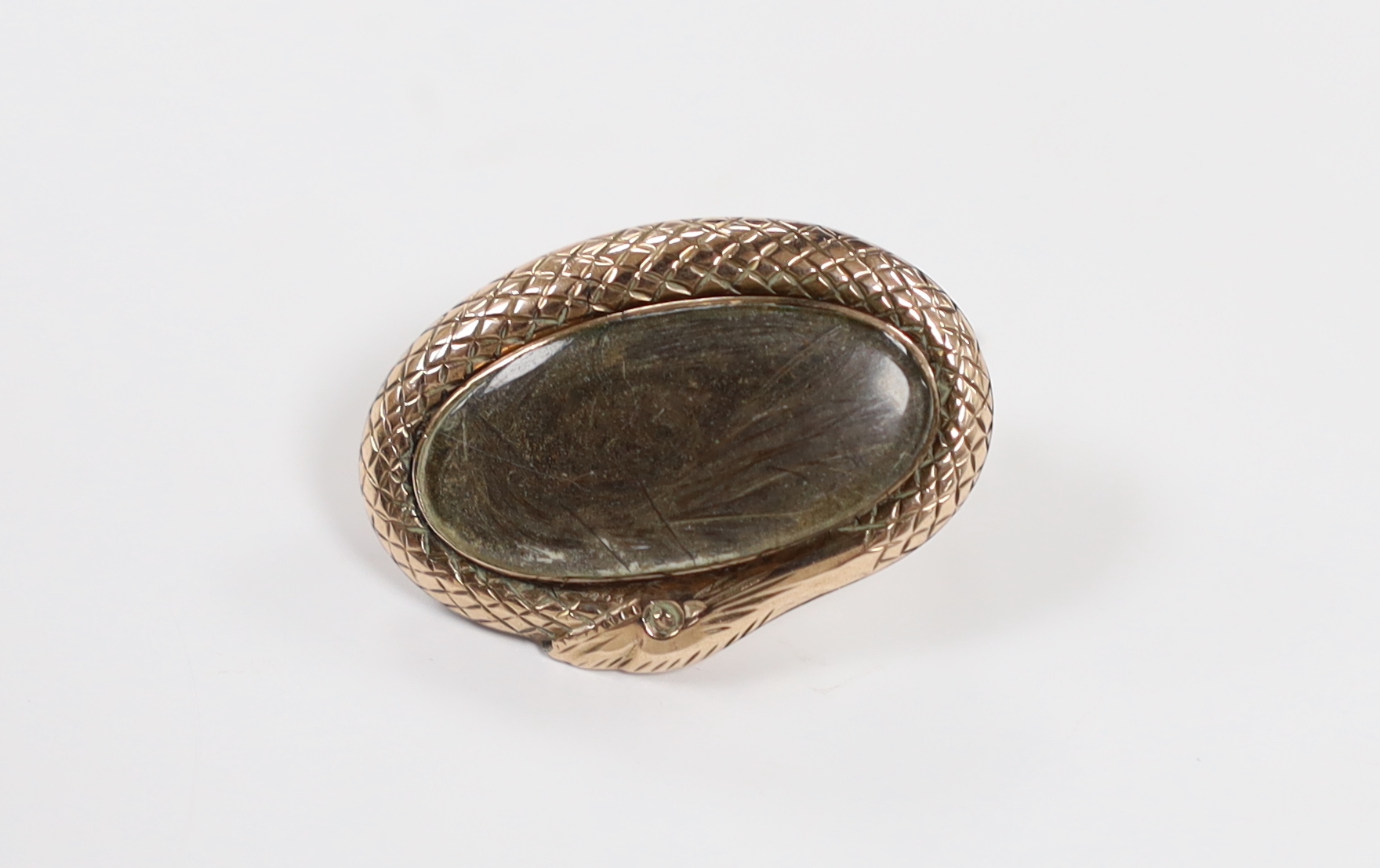 A Victorian yellow metal mounted oval mourning brooch, with plaited hair beneath a glazed panel and serpent border, 25mm.